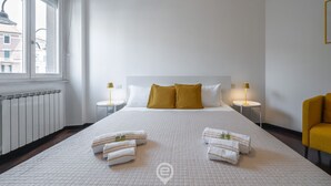 A hotel room with a large bed, two bedside tables with lamps, a window with blinds, and a view of buildings outside. - Comfort Corner in Via Dante (Cagliari)