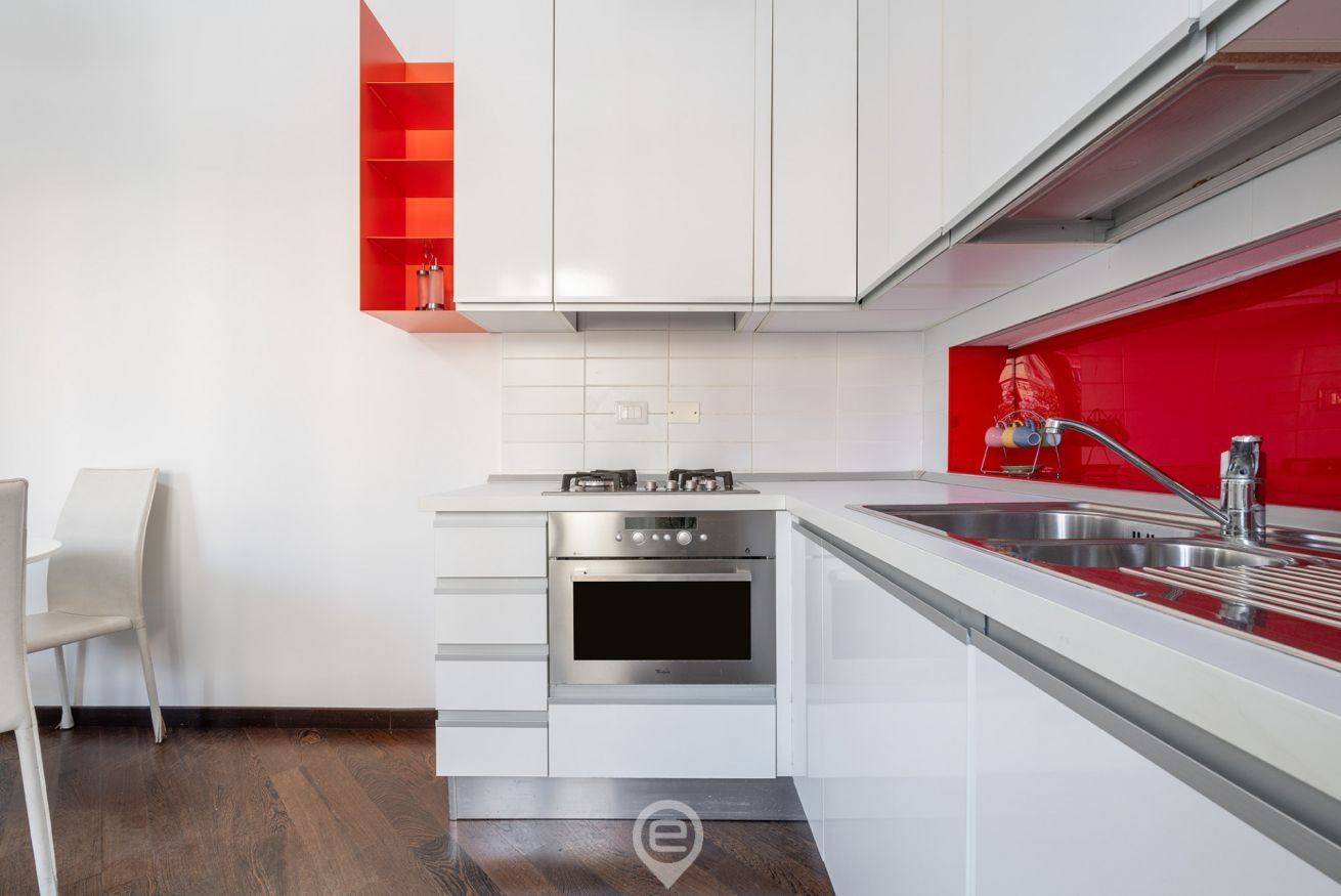 A modern kitchen with white cabinetry, a red backsplash, and stainless steel appliances.