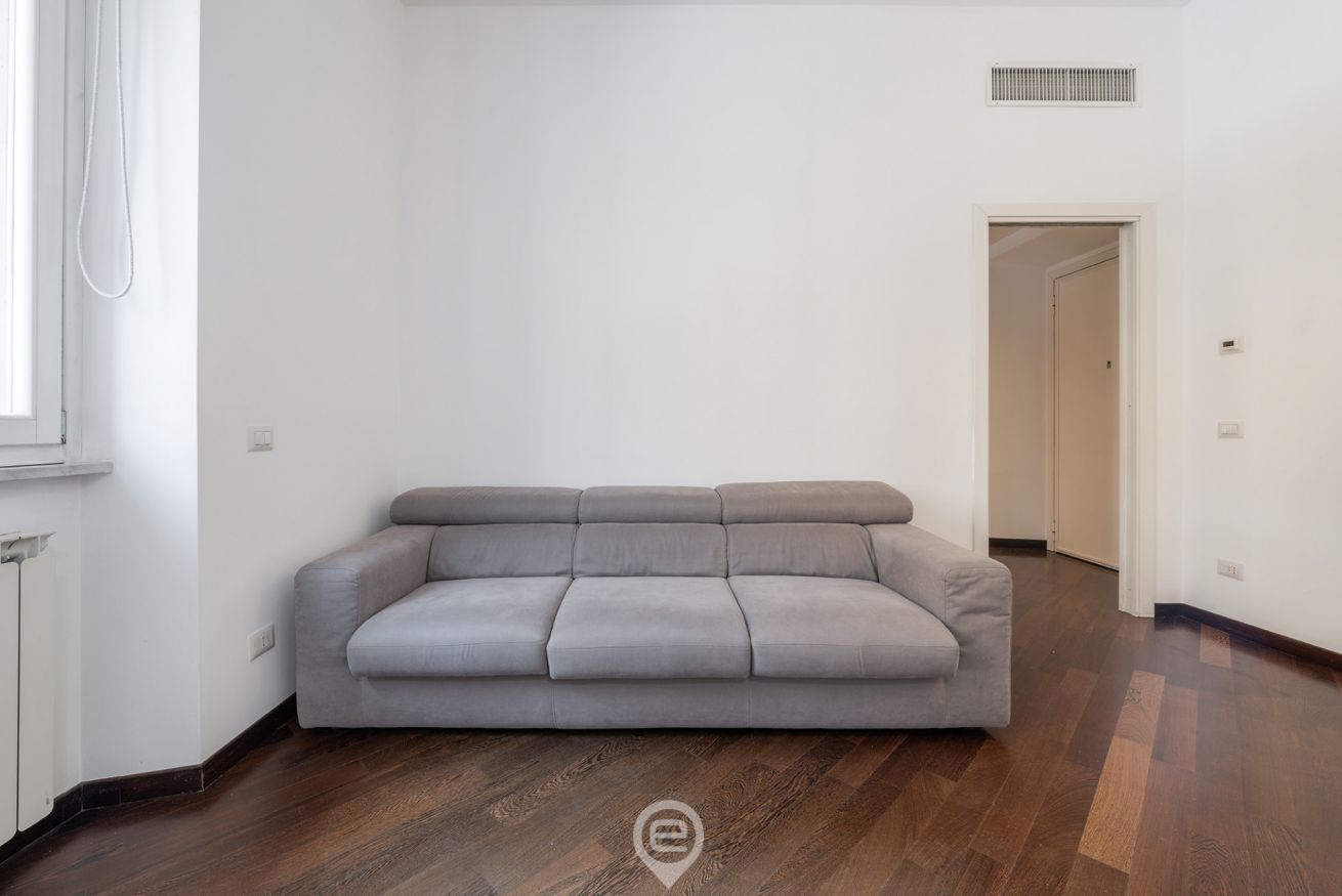 Un salon aux couleurs neutres, avec un canapé gris, un parquet en bois et un mur blanc.