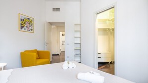 Ein Hotelzimmer mit einem Bett, einem gelben Sessel, einer weißen Wand mit einem gerahmten Bild und einem begehbaren Kleiderschrank.