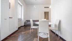 Ein moderner Essbereich mit einem runden Tisch, weißen Stühlen, einem grauen Sofa und Holzboden.