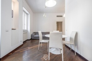 Zona pranzo moderna con un tavolo rotondo e sedie bianche, un divano grigio e un pavimento in legno.