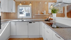 Een moderne keuken met witte kasten, een inbouwvaatwasser en een raam met uitzicht op een huis.