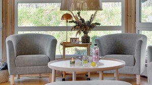 Een kamer met twee grijze fauteuils, een ronde witte tafel met een lamp, een vaas met gedroogde planten en een flesje met de tekst 'ENERGI'.