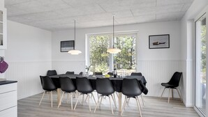 Un comedor moderno con una mesa grande, sillas negras, lámparas colgantes y vistas a árboles a través de un ventanal.