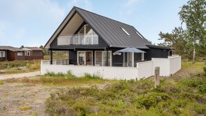 Una casa moderna de dos pisos con un balcón grande, rodeada por un paisaje natural.