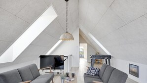 Un loft moderno con techos altos, un televisor grande y una zona de estar acogedora con sofás y una mesa de centro.