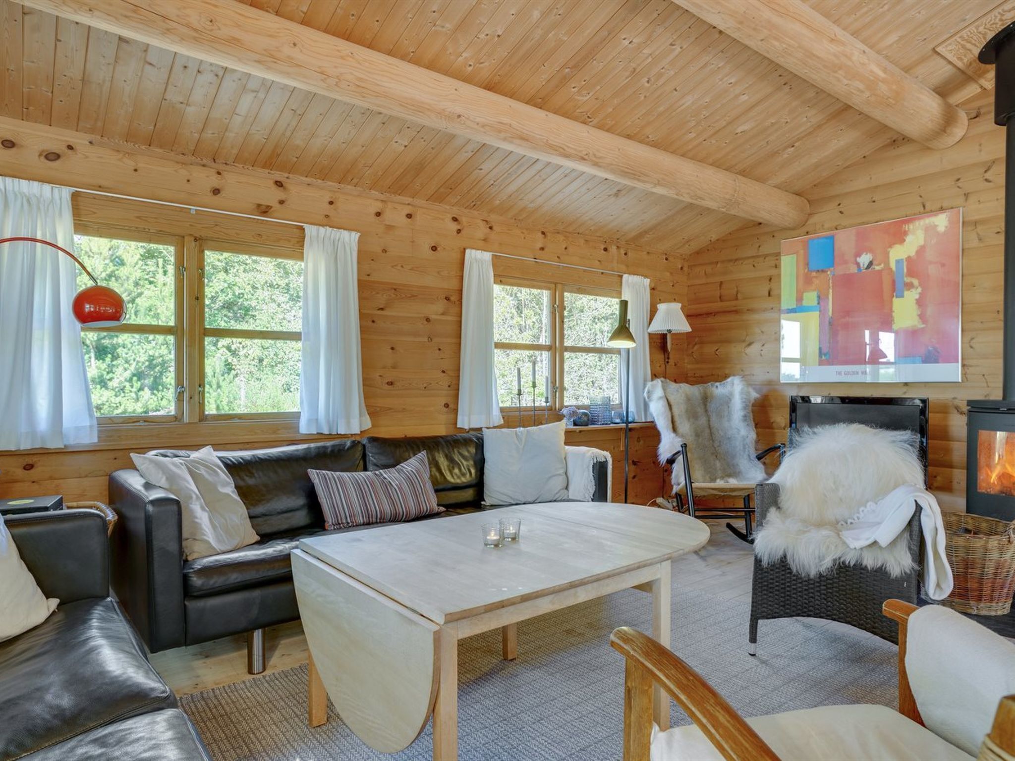 Een gezellig interieur van een blokhut met een houten plafond, een bank, een tafel en een open haard.