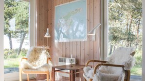 Une pièce aux murs en bois, une carte accrochée au mur, deux fauteuils recouverts de peaux de bêtes, une table et une lampe.