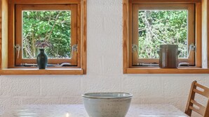 Un'area pranzo con tavolo, due candele e una ciotola. Due finestre con stipiti in legno, ognuna con un vaso e una pianta.