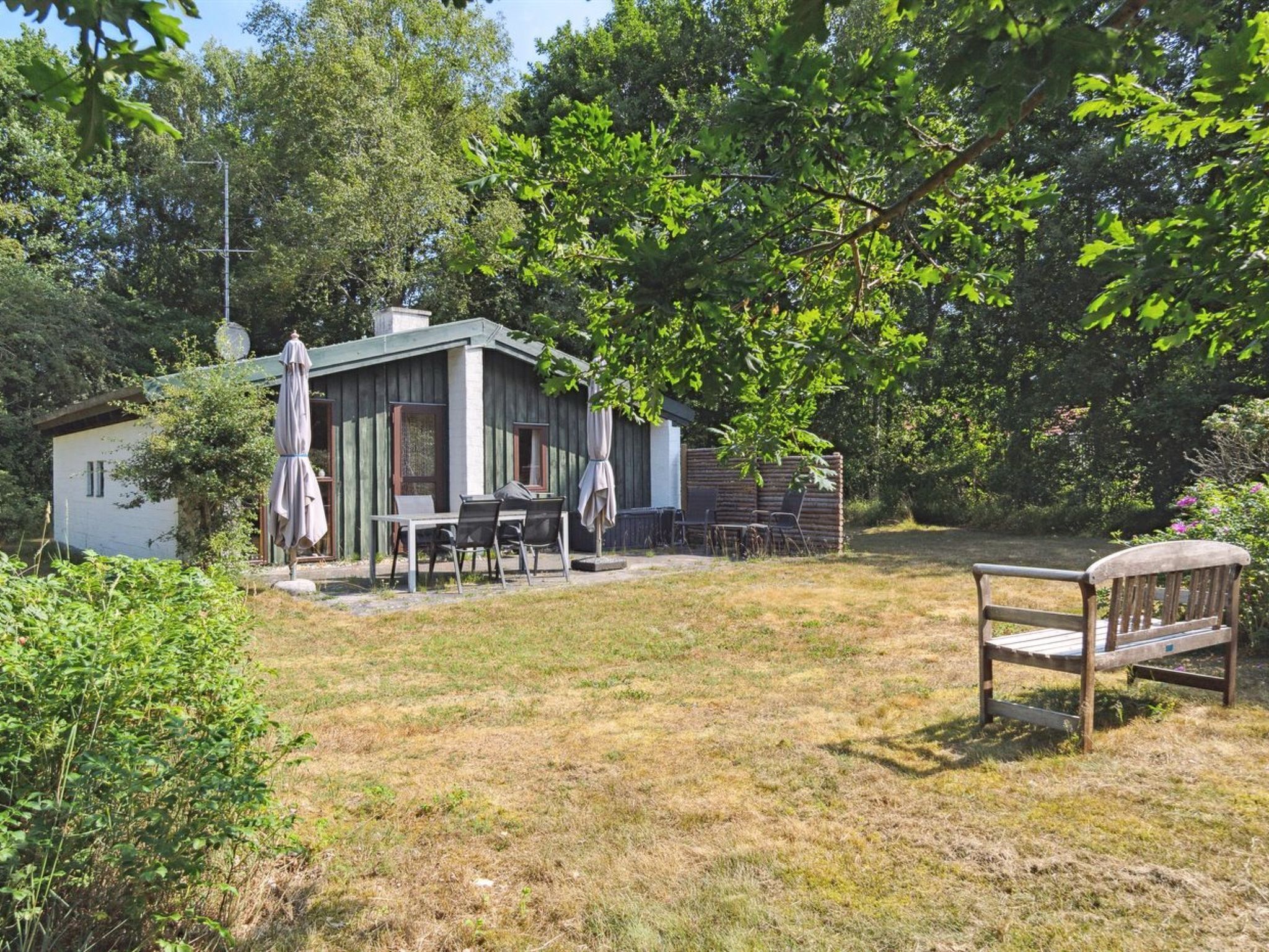 A rustic cabin with a dining area, surrounded by trees and a grassy yard.