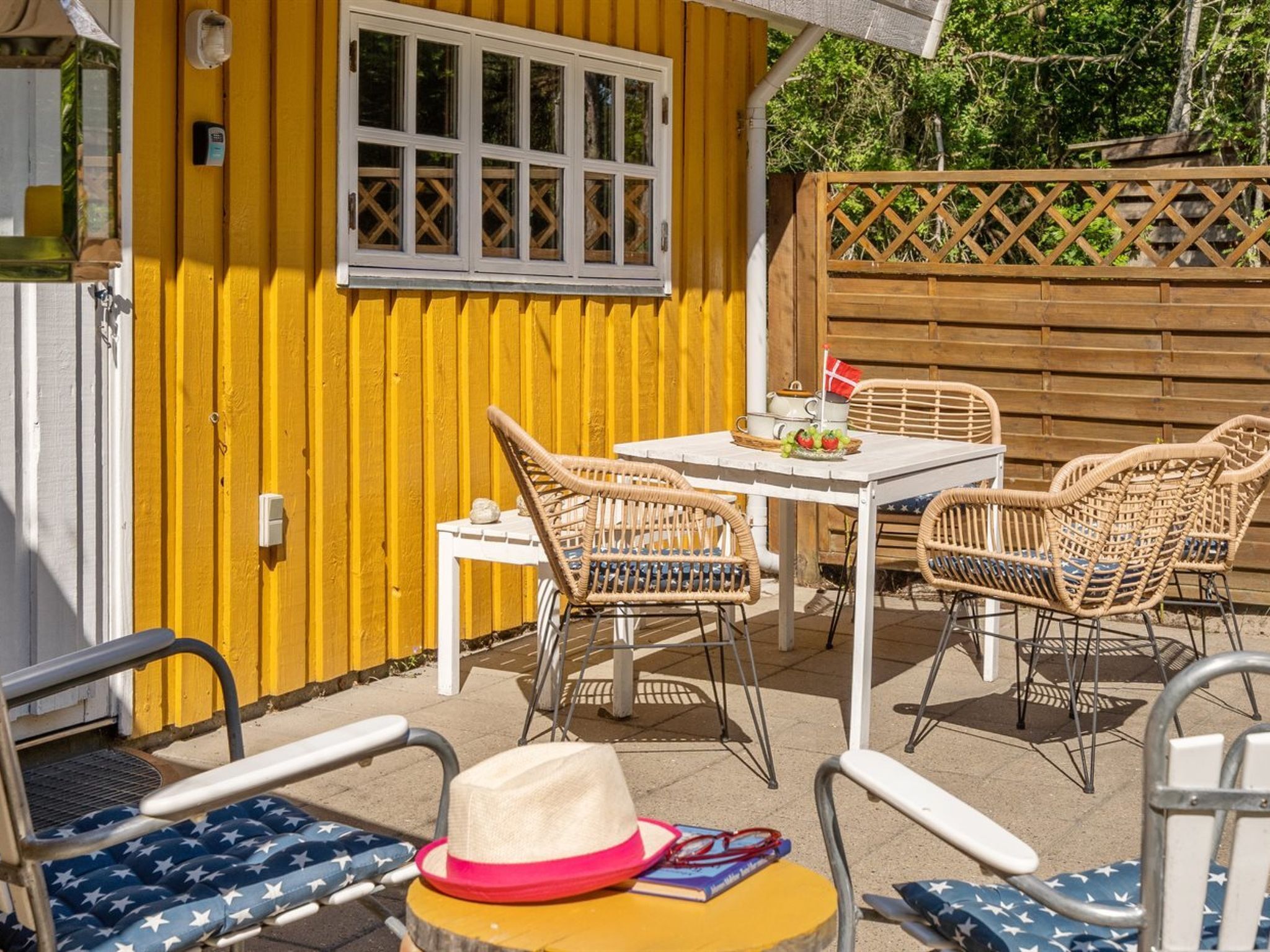A yellow building with a white window and a white door. There is a table with chairs and a hat on the table.