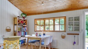 A cozy dining area with a wooden ceiling, white paneled walls, a large window, and a bookshelf filled with books. - "Mirla" - 300m from the sea by Interhome (Læsø)
