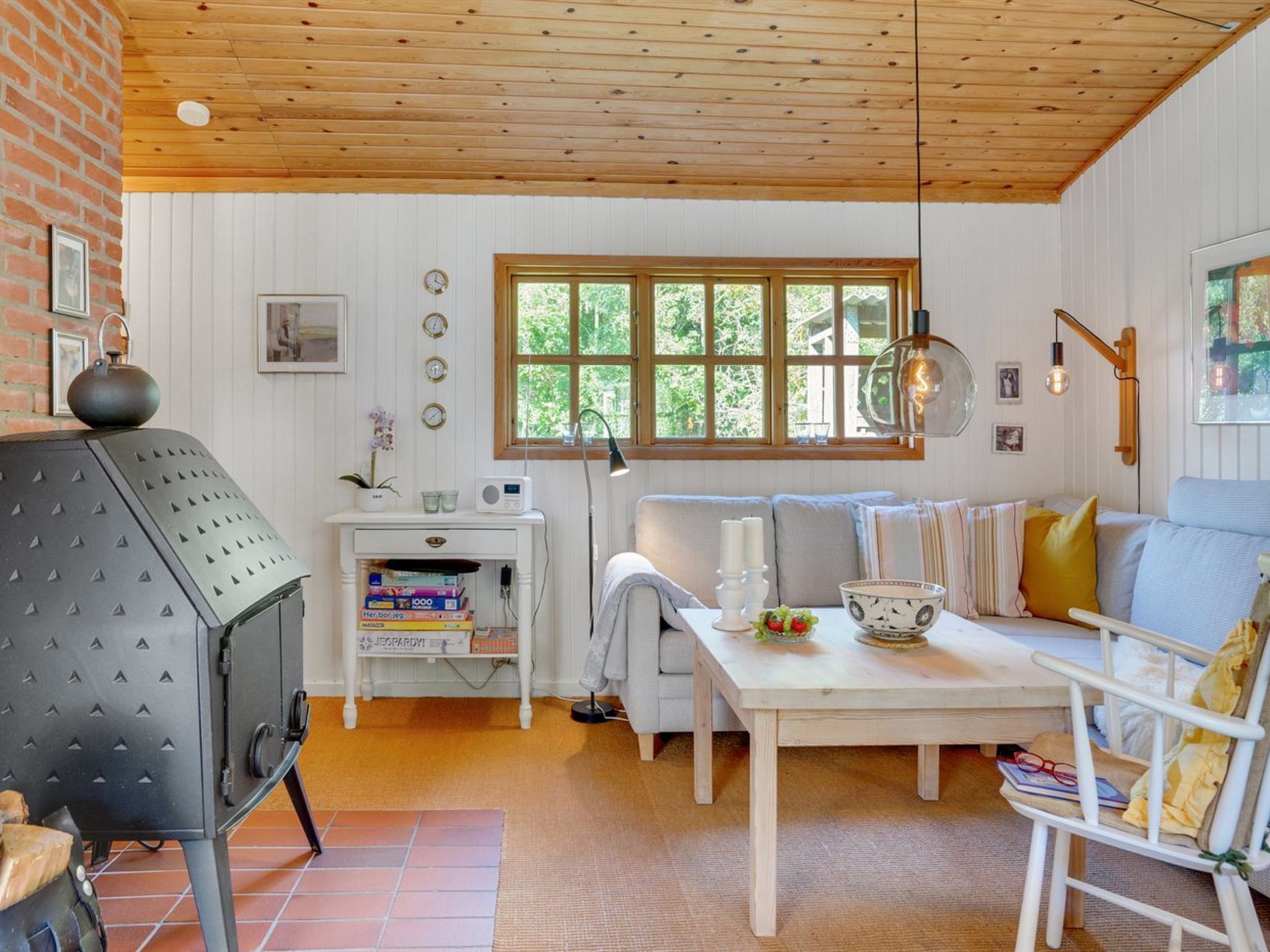 Una sala de estar acogedora con chimenea, un sofá, una mesa con velas y una ventana con vistas a follaje.
