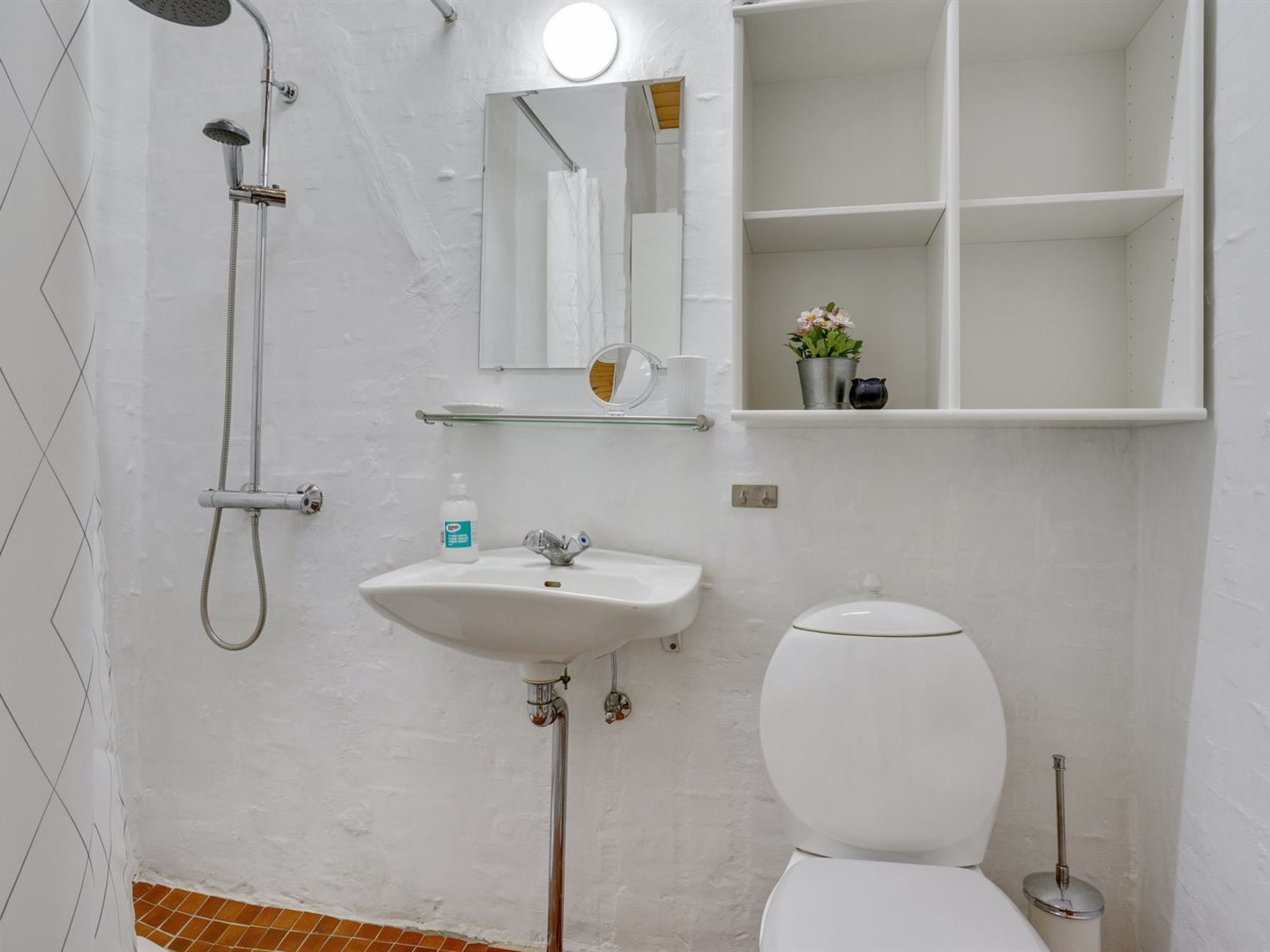 Een badkamer met douche, wastafel, toilet en spiegel.