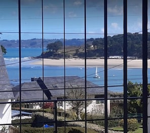A coastal view through a window with a grid pattern, featuring a beach, ocean, and distant hills.