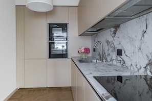 A modern kitchen with a built-in oven, a marble backsplash, and a stainless steel sink.