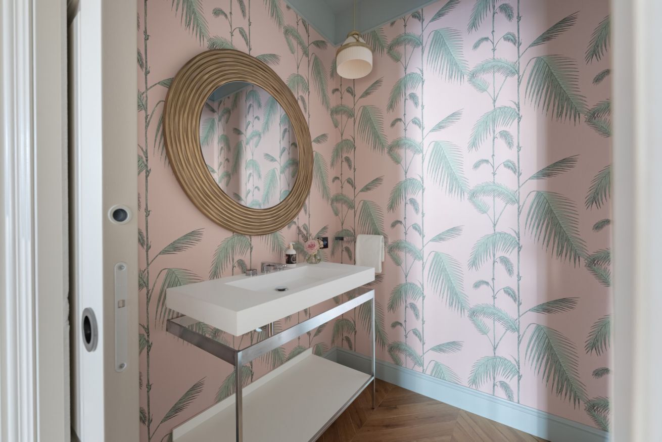 A bathroom with a white sink, a round mirror, and a wall with a palm leaf pattern.