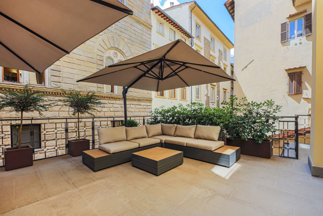 Un espace extérieur aménagé avec un canapé d’angle, une table basse et un grand parasol.