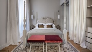 A bedroom with a large bed, two bedside tables, a red bench, and a patterned rug.