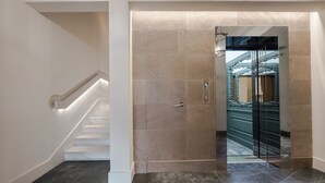 A modern interior with a marble staircase, a glass elevator, and a tiled wall.