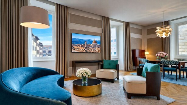 A modern living room with a large TV, comfortable seating, a round coffee table, and a view of a cityscape through large windows.