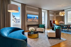 A modern living room with a large TV, comfortable seating, a round coffee table, and a view of a cityscape through large windows.