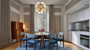 A dining area with a round table, six chairs, a chandelier, and a kitchen with modern appliances.