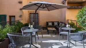 An outdoor patio with wicker furniture, a table with a vase of flowers, and a large umbrella providing shade.