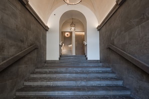 Eine imposante Treppe mit Steinwänden und einem Chandelier, die zu einer Tür mit einer runden Leuchte führt.