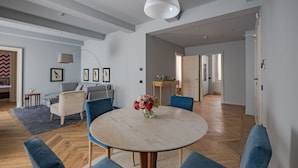 A spacious living area with a round table, blue chairs, a sofa, and a dining table with a vase of flowers. - Apartments Florence -Palazzo Signoria Luxury Apartments 7-Perseo (FIRENZE)