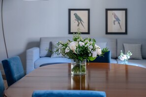 Et spisebord med en blomstervase, en blå stol og en grå sofa i baggrunden.