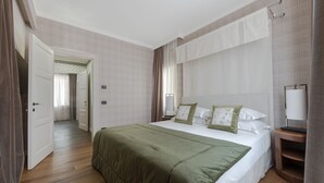 A hotel room with a large bed, a bedside table, a nightstand, a lamp, and a door leading to another room. - Apartments Florence - Palazzo Signoria Luxury Apartments 11- Medusa (Firenze)