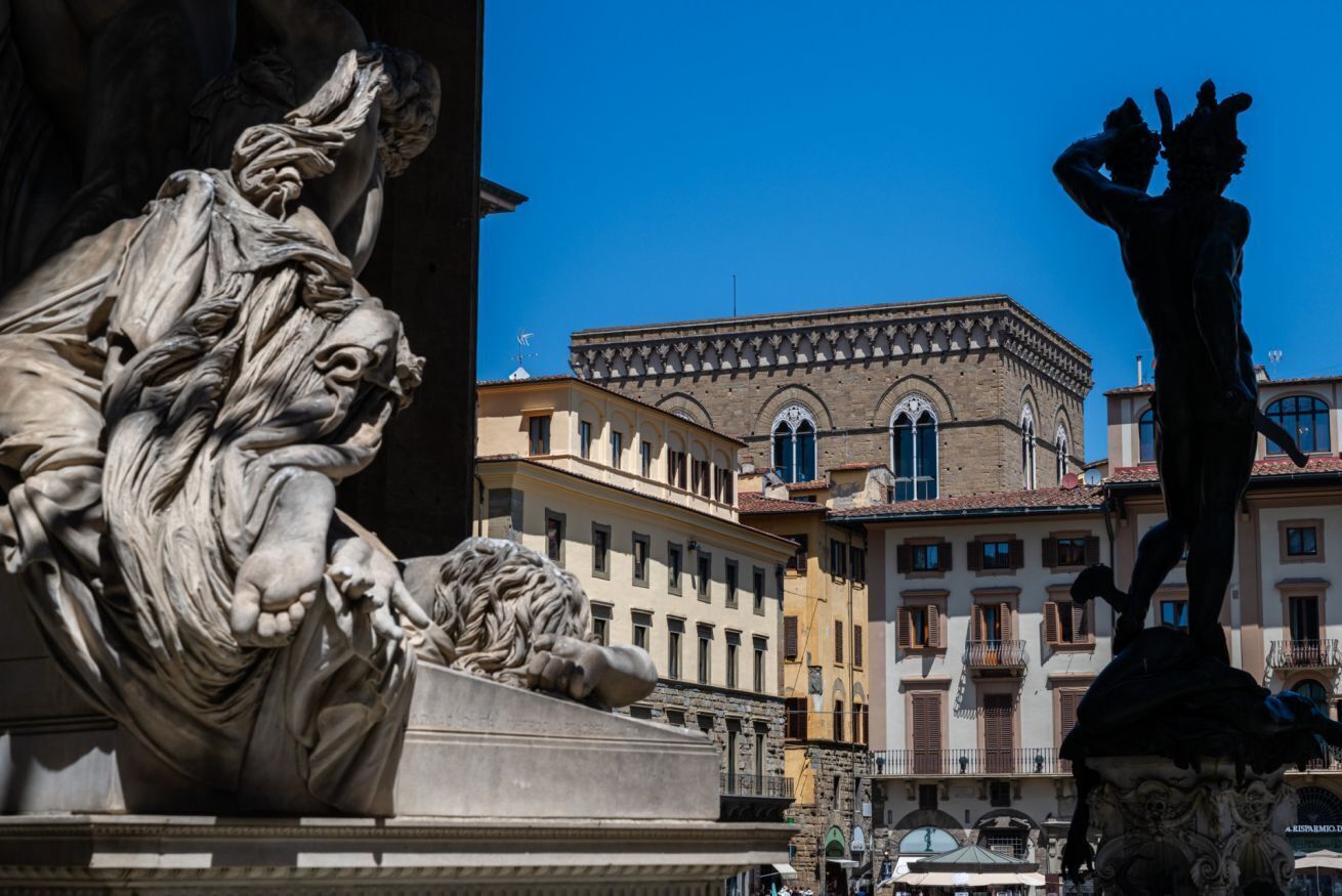 A statue of a man with a raised arm, a lion, and a building with arched windows in the background.