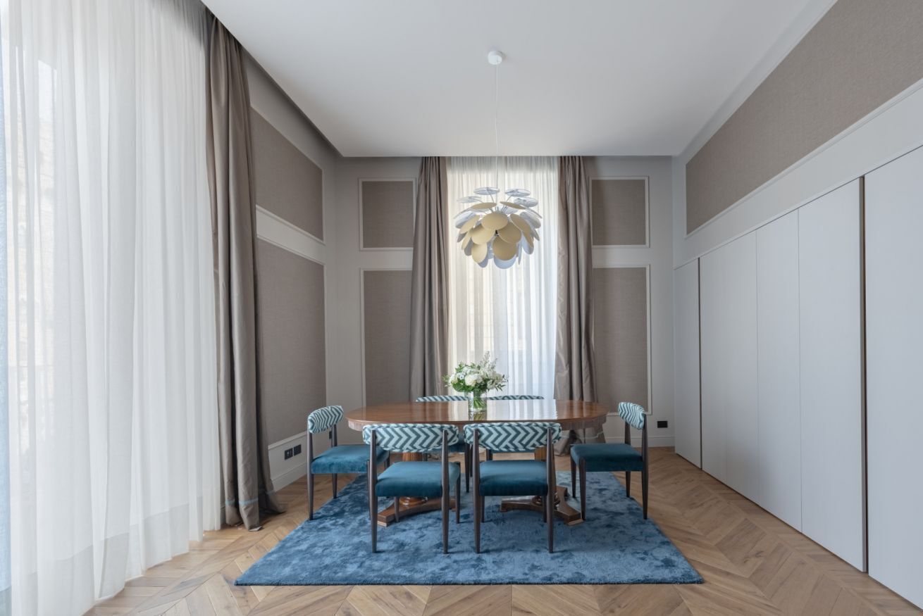 A dining area with a round table, six chairs, a blue rug, and a decorative light fixture.