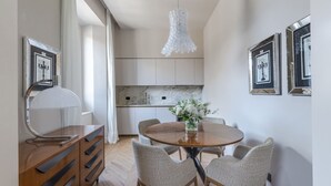 Un espace repas moderne avec une table ronde en bois, six chaises en osier, un lustre et des œuvres d’art encadrées accrochées aux murs.