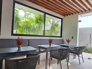 Un espace repas doté d’une grande fenêtre, de poutres en bois au plafond et de deux tables accompagnées de chaises.