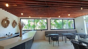 Un interno moderno con soffitto in legno, ampie finestre vista su vegetazione, un bancone con bicchieri e zone relax.