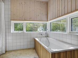 Une salle de bain moderne avec une baignoire, un lambris en bois et trois fenêtres donnant sur un paysage verdoyant.