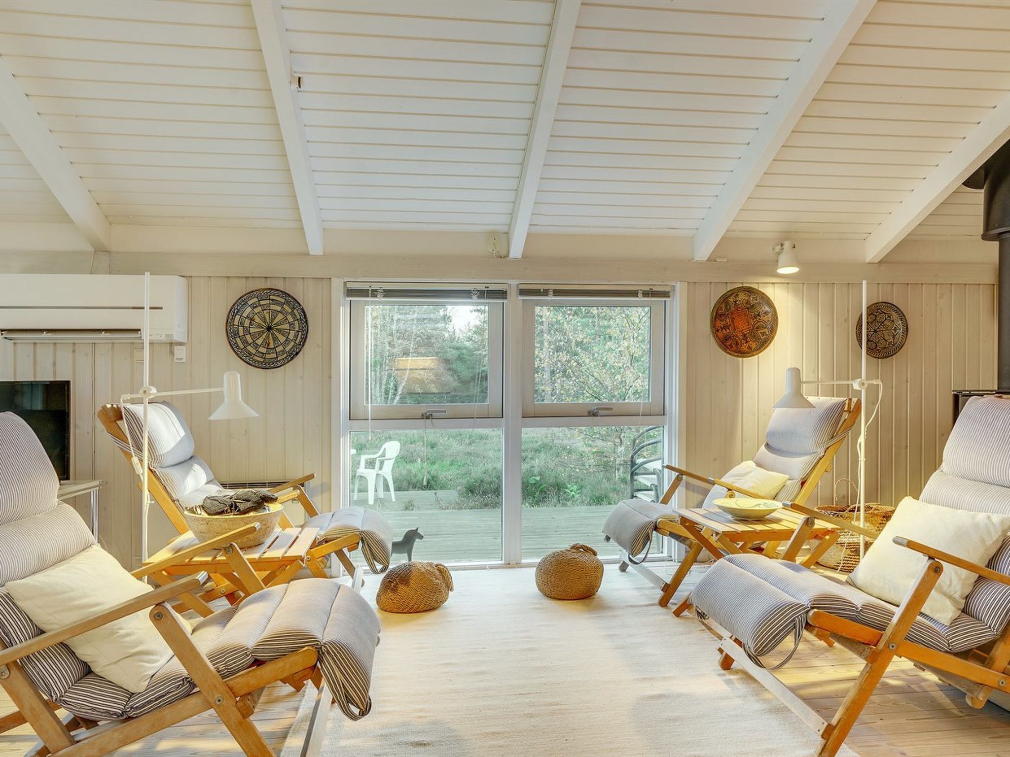A sunlit room with wooden chairs, a television, and a large window overlooking greenery.