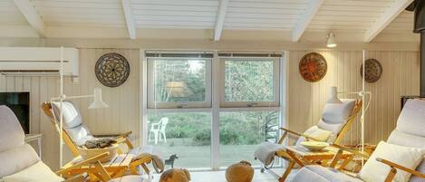 A sunlit room with wooden chairs, a television, and a large window overlooking greenery.