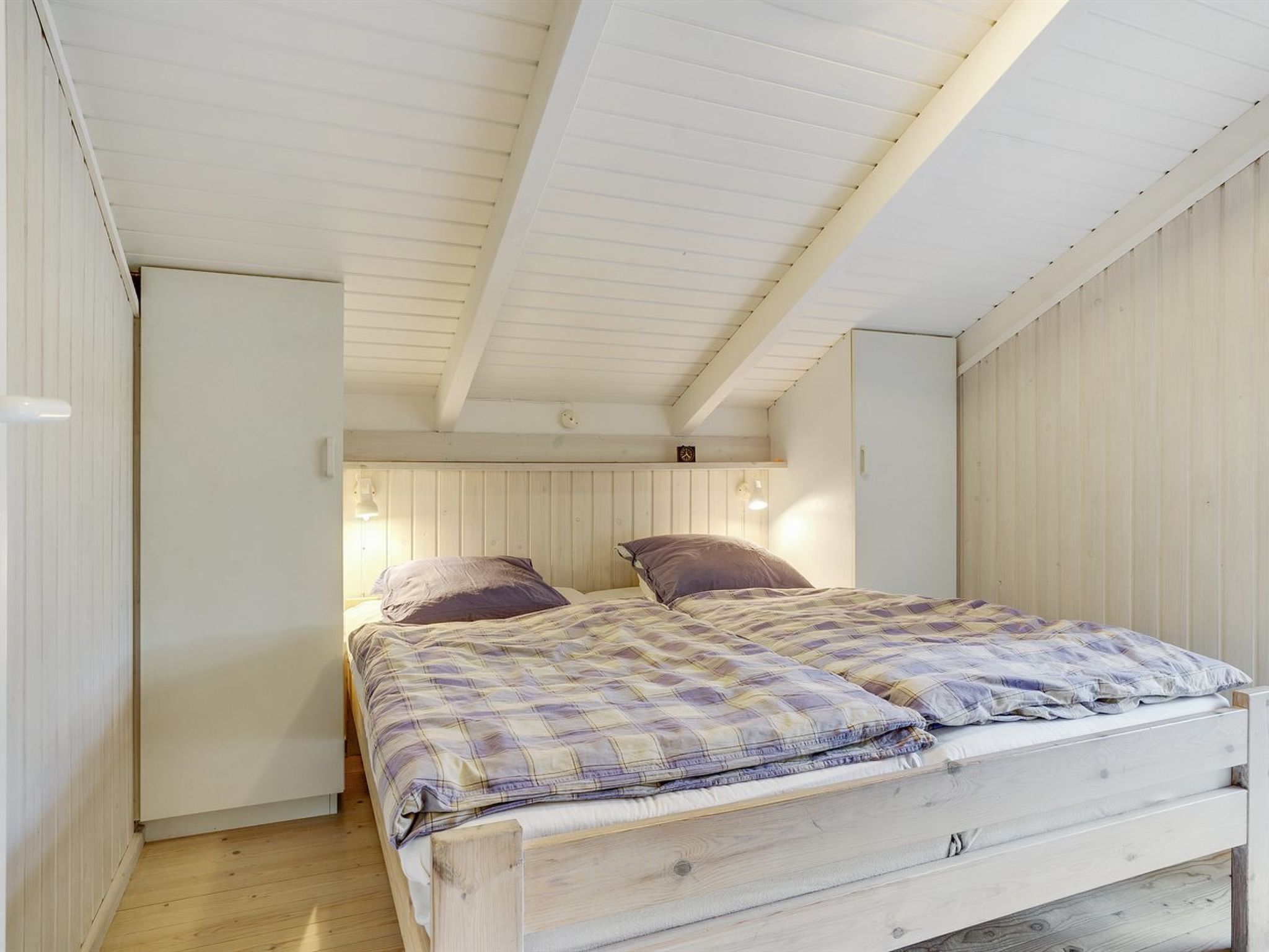 Een slaapkamer met een houten bed, twee bedlampen en een witte garderobe.