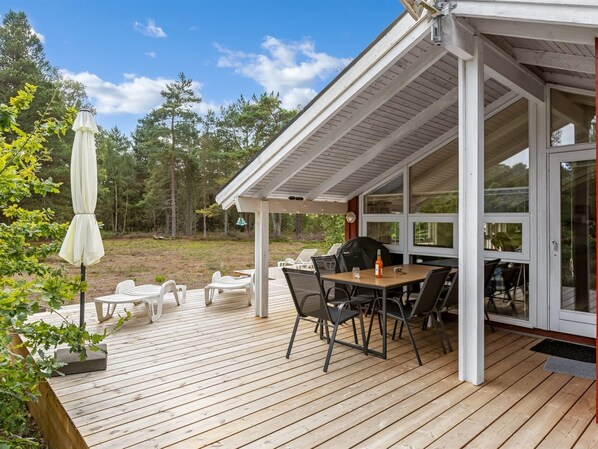 A covered outdoor patio with a table and chairs, a grill, and a white umbrella.