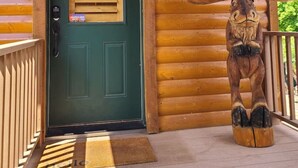 Una cabaña de madera con puerta verde, buzón, soporte para buzón y una escultura de madera en el porche.