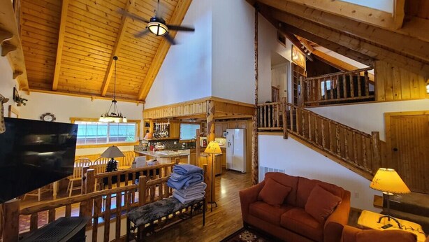 Un salón amplio con techo alto, vigas de madera, una escalera y una zona de estar acogedora.