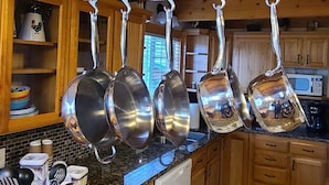 Una cocina con armarios de madera, encimera de granito y ollas colgantes.