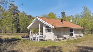 Ein eingeschossiges Blockhaus mit roten Ziegeln, einer Veranda mit Tisch und Stühlen sowie einer Satellitenschüssel auf dem Dach.