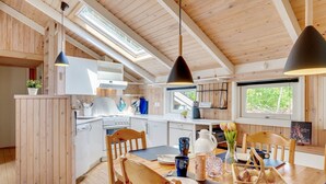 Eine moderne Küche mit Holzelementen, ein Essbereich mit Tisch und Stühlen sowie ein großes Fenster, das für natürliches Licht sorgt.