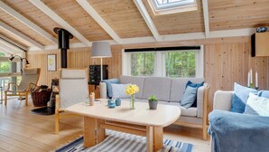 Ein gemütliches Blockhaushaus-Interieur mit Holzbalkendecke, einer Couch, einem Tisch und einem Kamin.