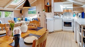Eine moderne Küche mit weißen Schränken, einem Herd und einem Spülbecken. Es gibt einen Essbereich mit einem Holztisch und Stühlen.